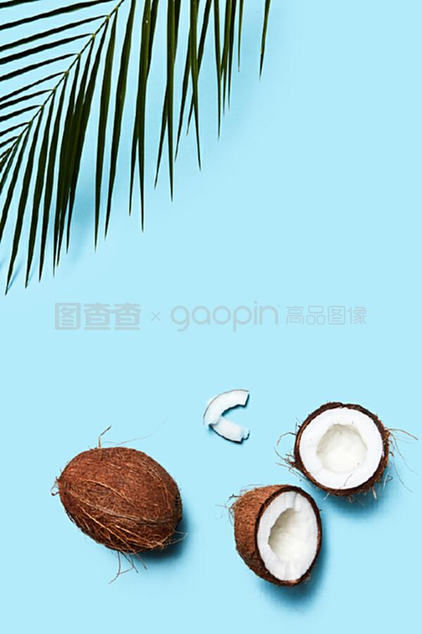 一片椰子和整個椰子,在藍色背景上有一片棕櫚綠葉。食物成分。平鋪。一個由有機的一半和一個椰子組成的美麗組成的藍色背景裝飾著一塊飾板,上面有一片平鋪。